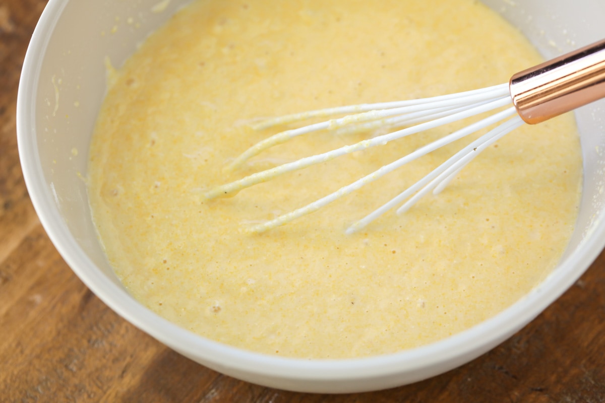 Sweet cornbread muffin batter in a white bowl with whisk.