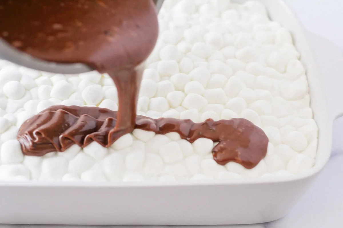 Frosting being drizzled over mini marshmallows in cake pan.