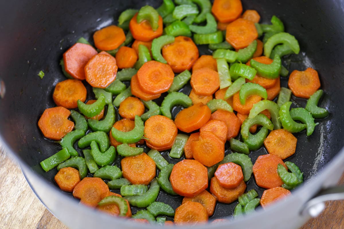 Carrots and celery being sautéed in a large pot.