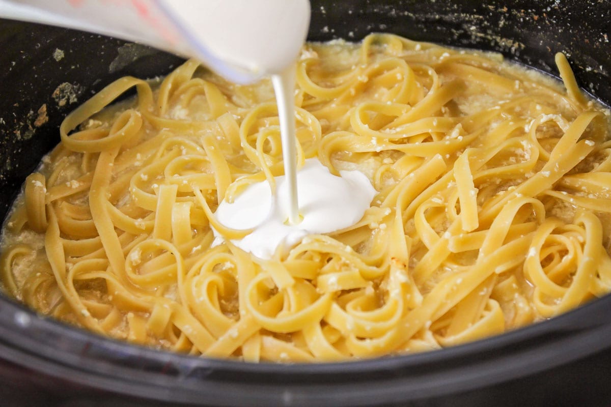 fettuccini noodles in a crock pot being covered in cream