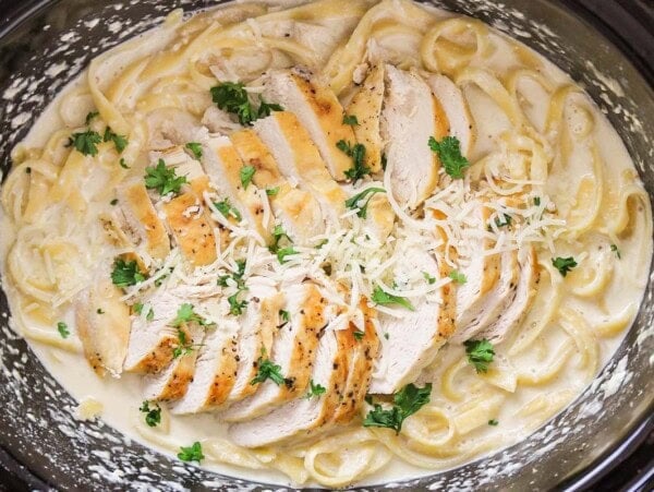 Crock pot chicken alfredo topped with cheese and fresh herbs.