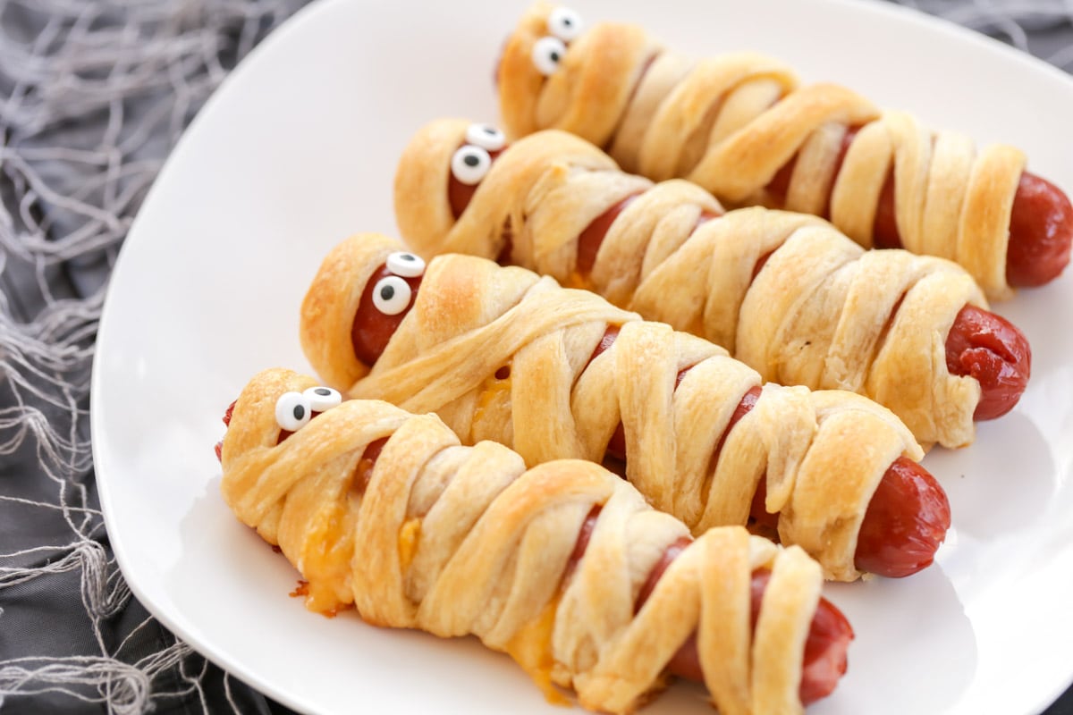 Mummy hot dogs with eyes on a white plate.