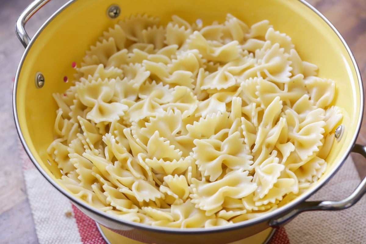 Bow tie pasta draining in a yellow colander.