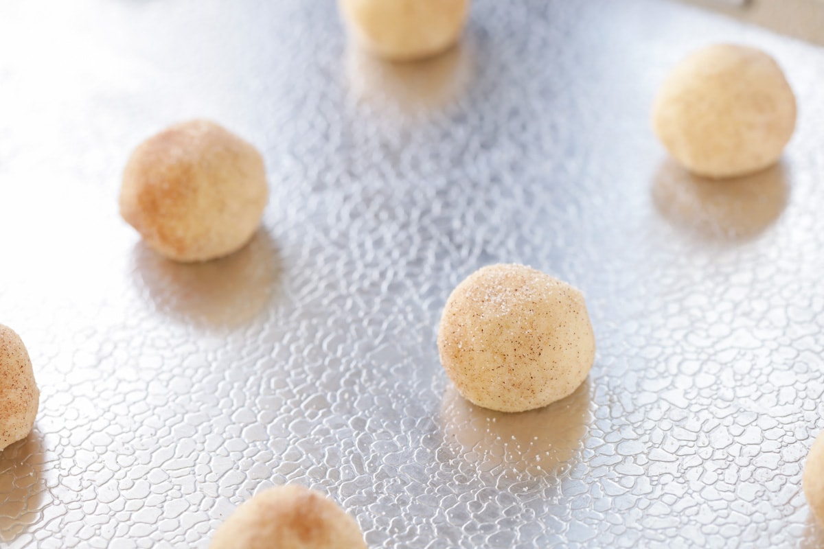Snickerdoodle balls dipped in cinnamon and sugar on a baking sheet