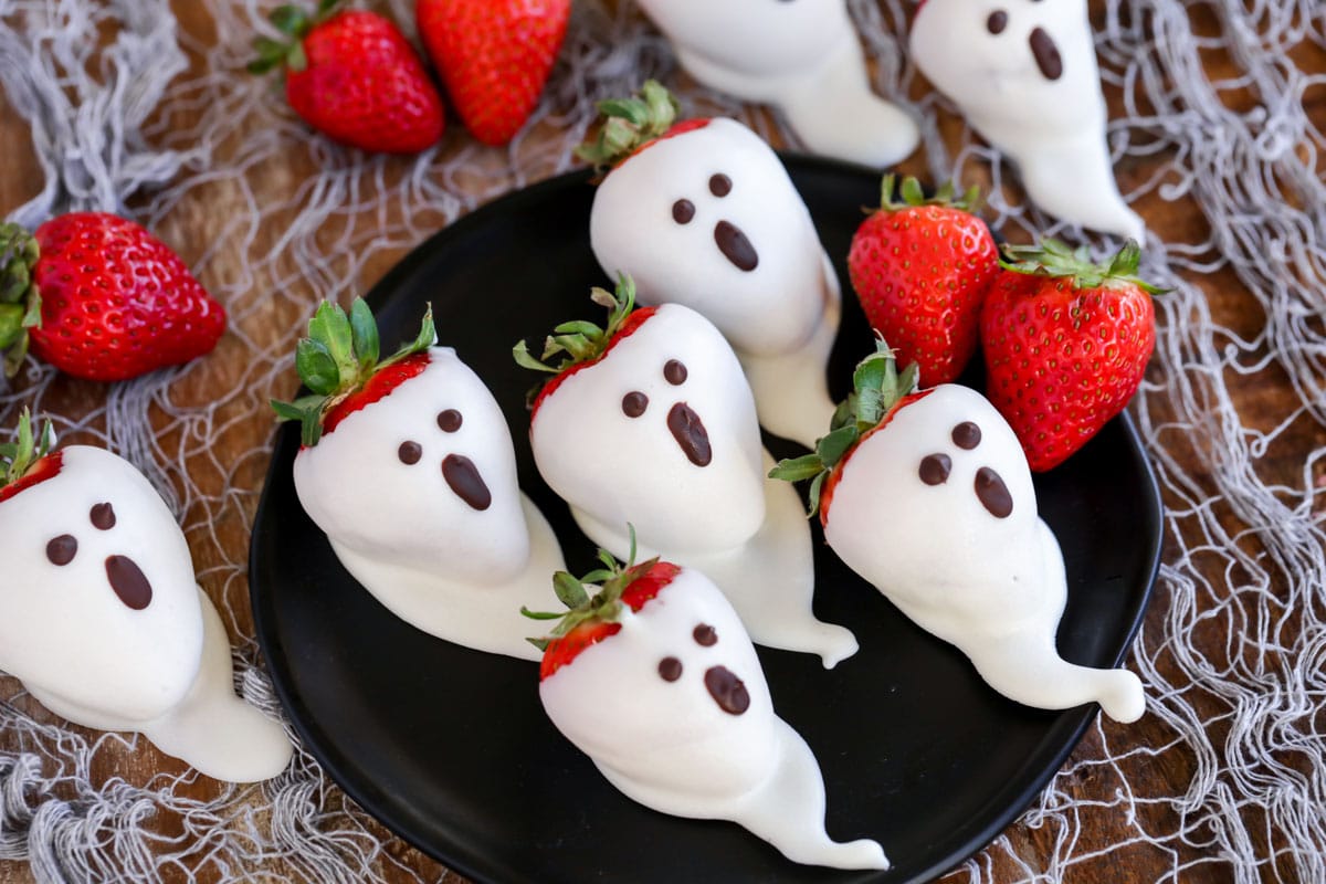 Dipped strawberry ghosts on a black plate