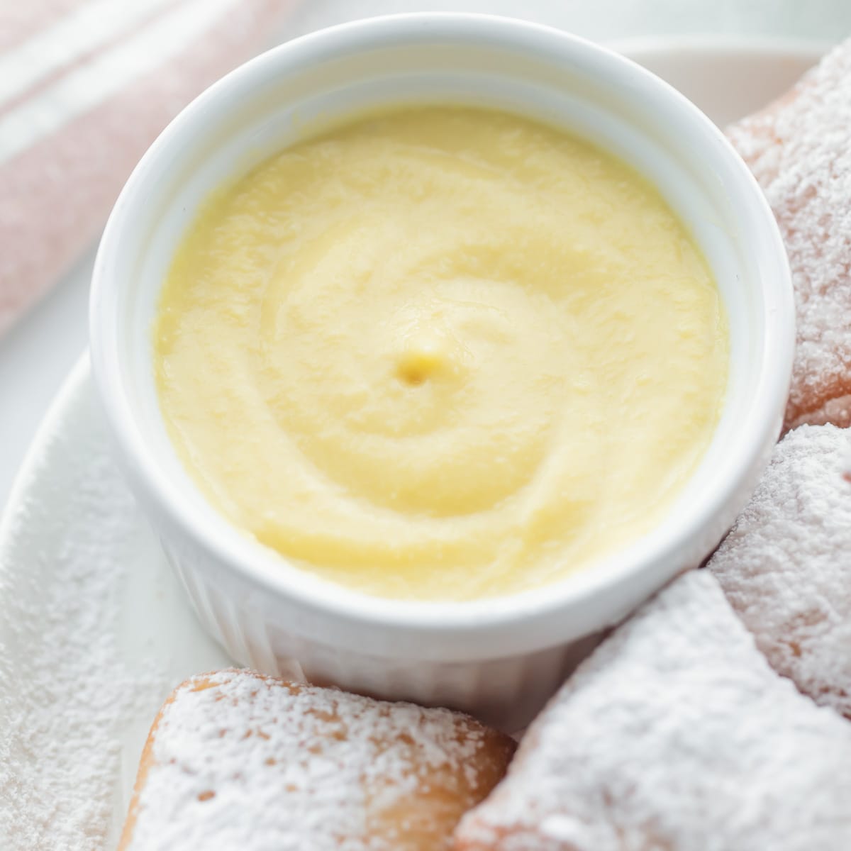 Vanilla crème anglaise in a white custard bowl served with beignets