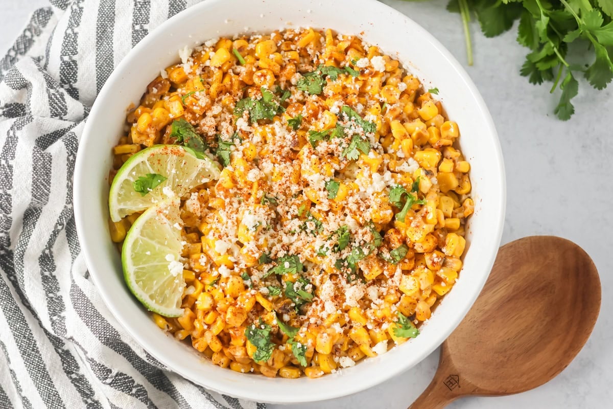 Esquites recipe served in a white bowl topped with cilantro, lime, Cotija and cilantro.