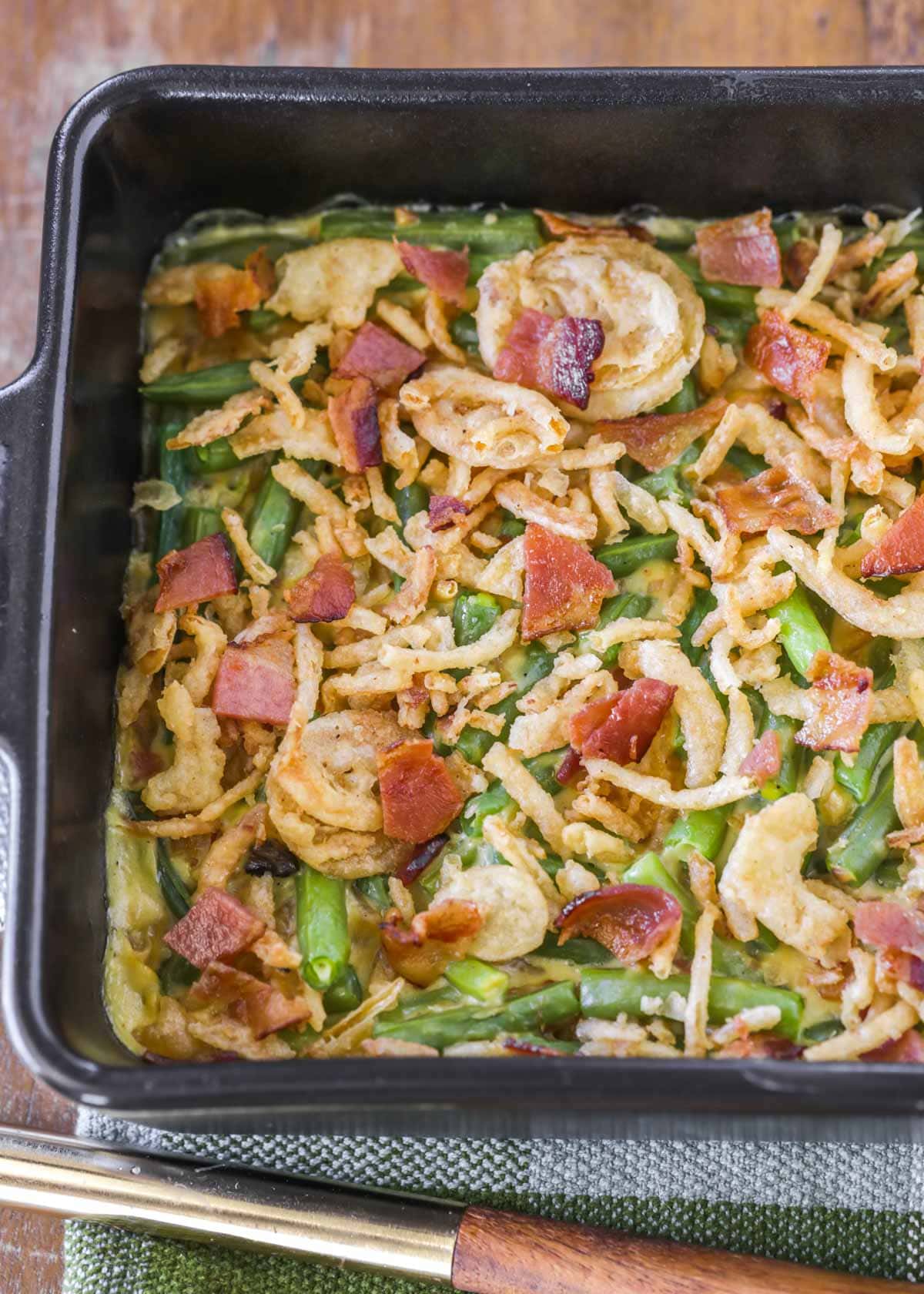 fresh green bean casserole with bacon topped with fried onions in a baking dish
