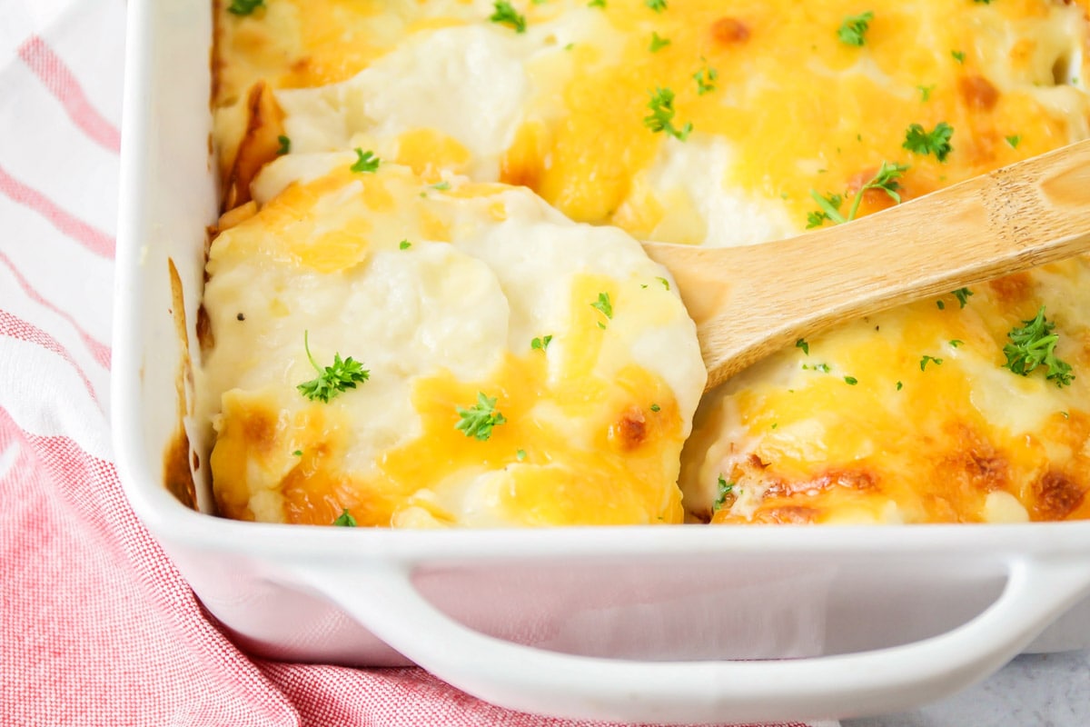 Scalloped potatoes with a wooden serving spoon.