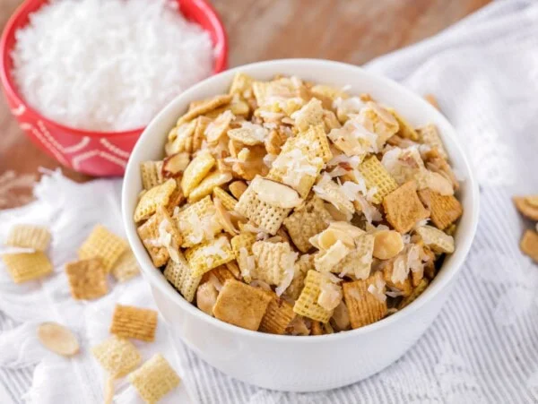 Sweet chex mix recipe in white bowl with ingredients around it.