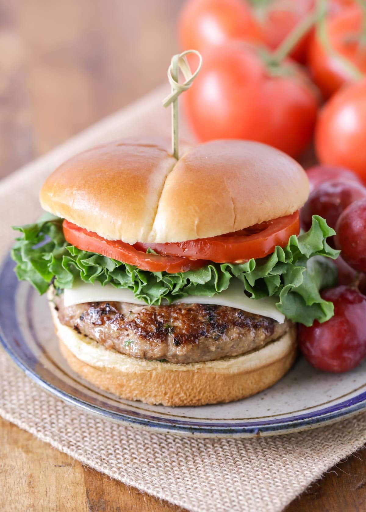 Turkey burger recipe on a bun with lettuce, tomato, and cheese served an a blue striped plate.
