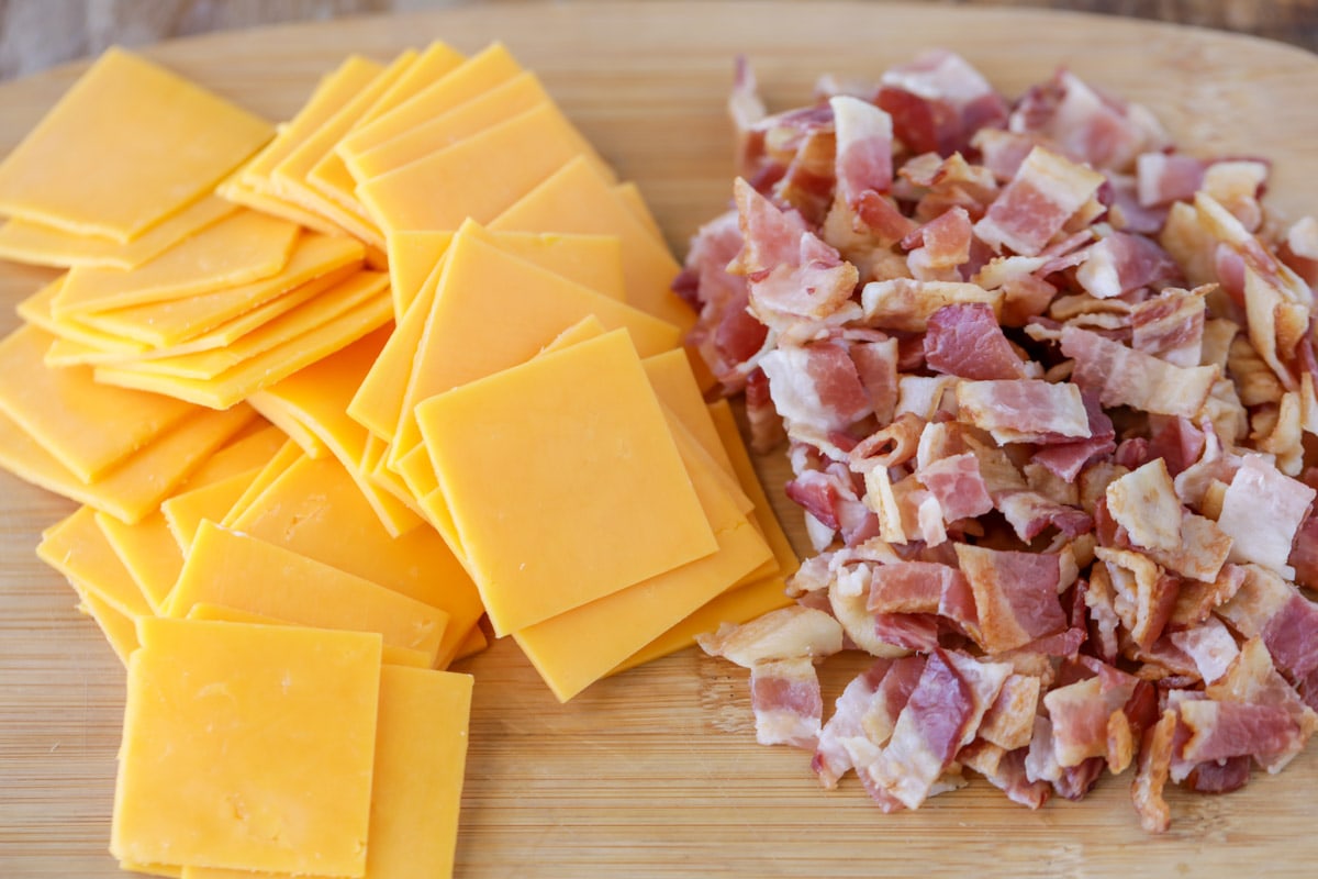 sliced of cheddar cheese and diced uncooked bacon on a cutting board