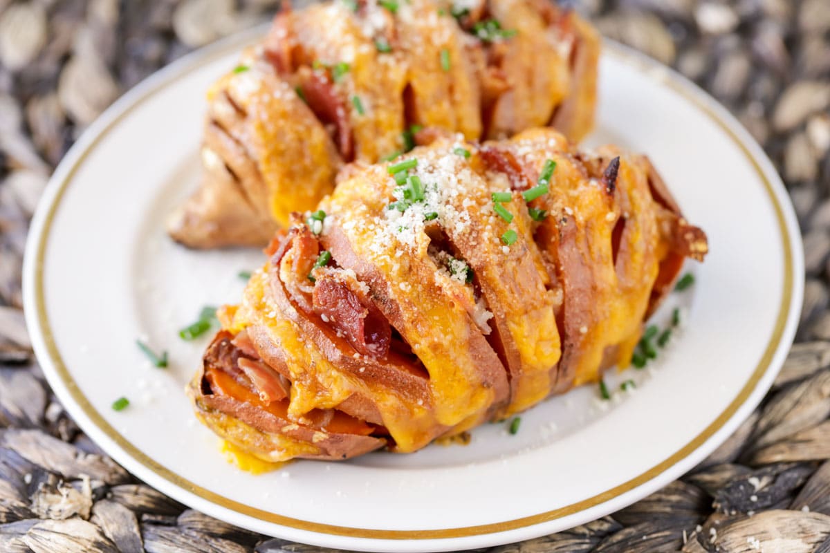 cheesy hasselback sweet potatoes on a white plate sprinkled with chives