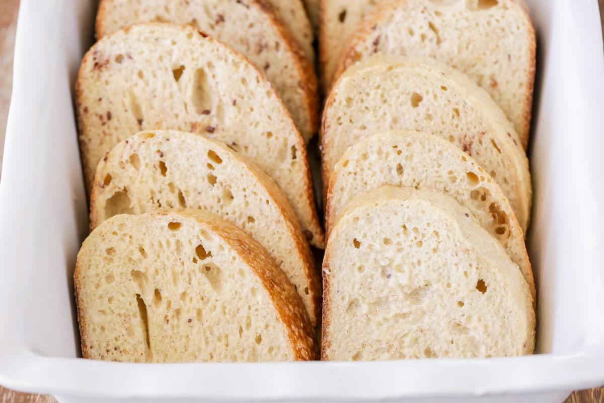 sliced french bread lining a white baking dish