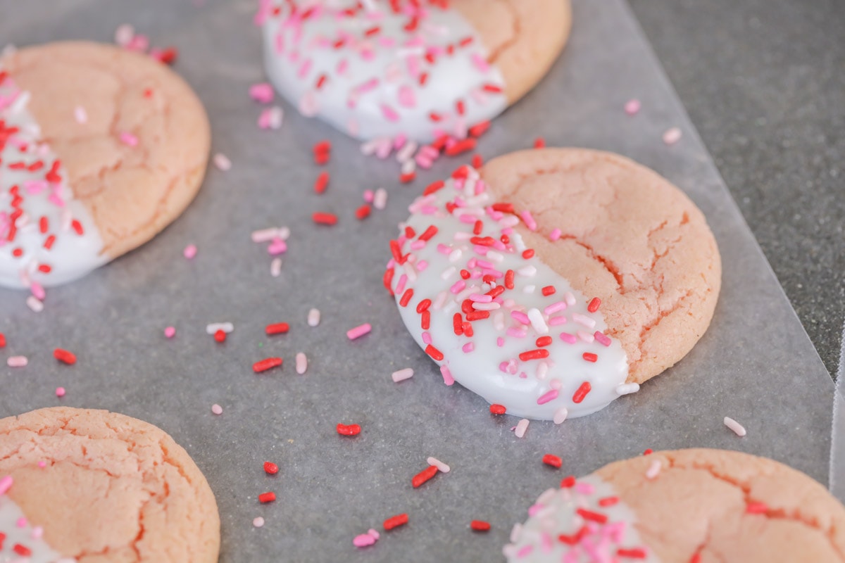 Sprinkled white chocolate dipped strawberry cookies on a sheet pan