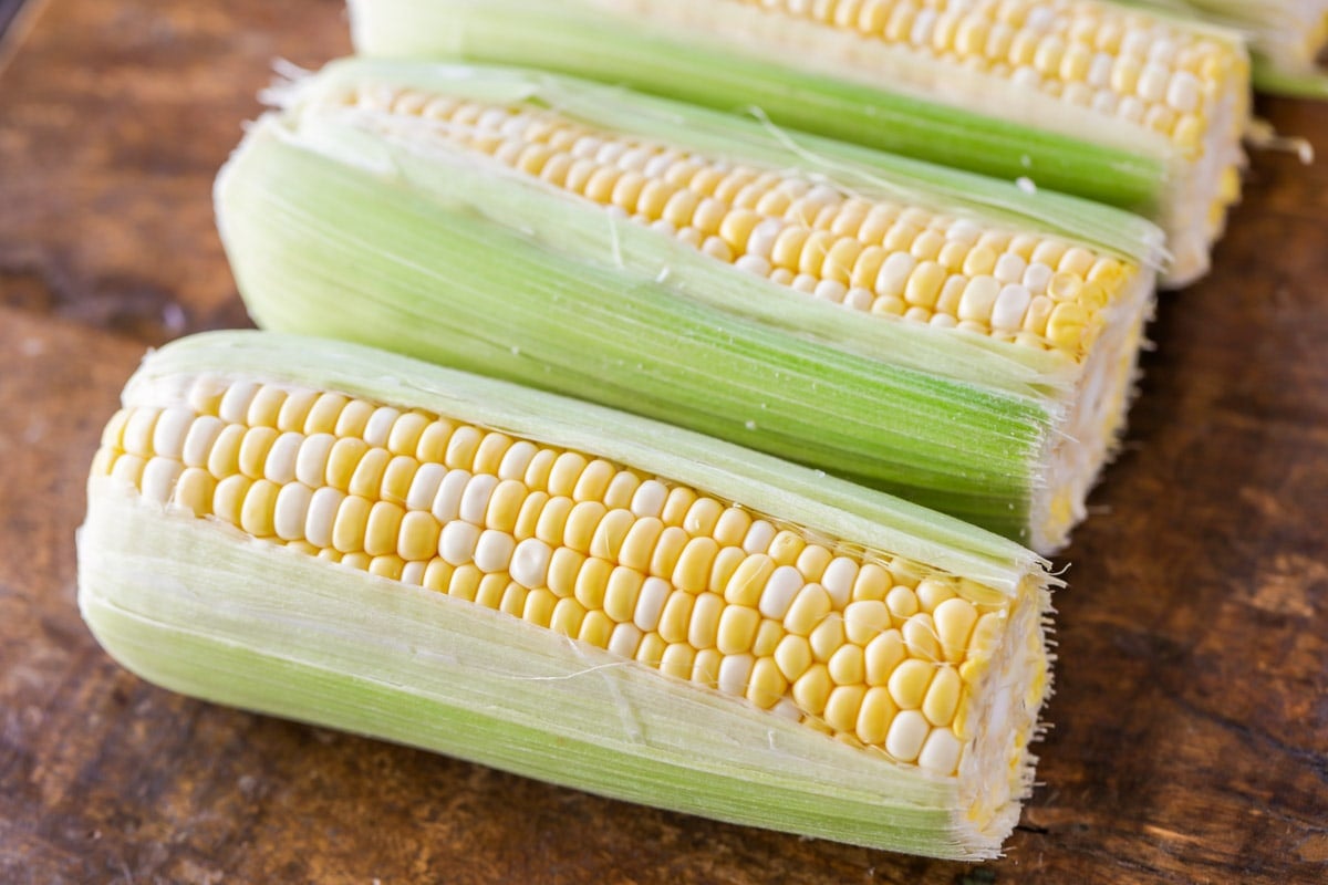 Fresh corn on the cob lined up on a wooden table.