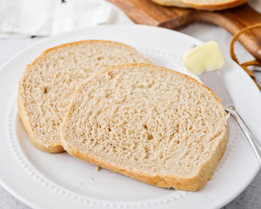 Two slices of wheat bread on a plate with a pat of butter
