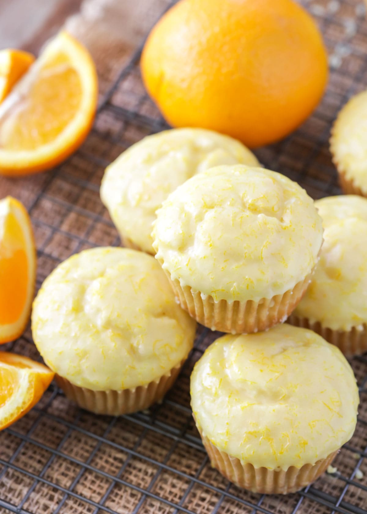 Orange muffins topped with glaze and stacked on a cooling rack.