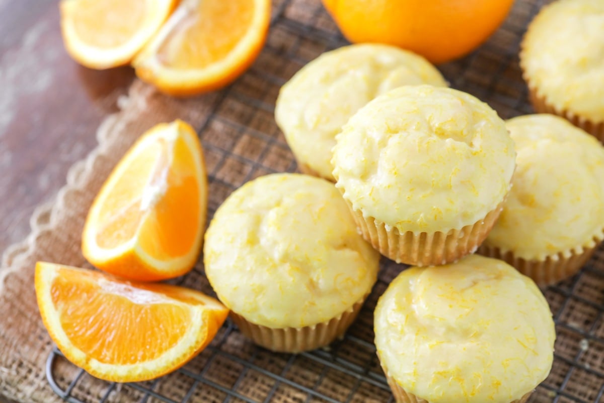 Orange muffins glazed and stacked on a cooling rack.