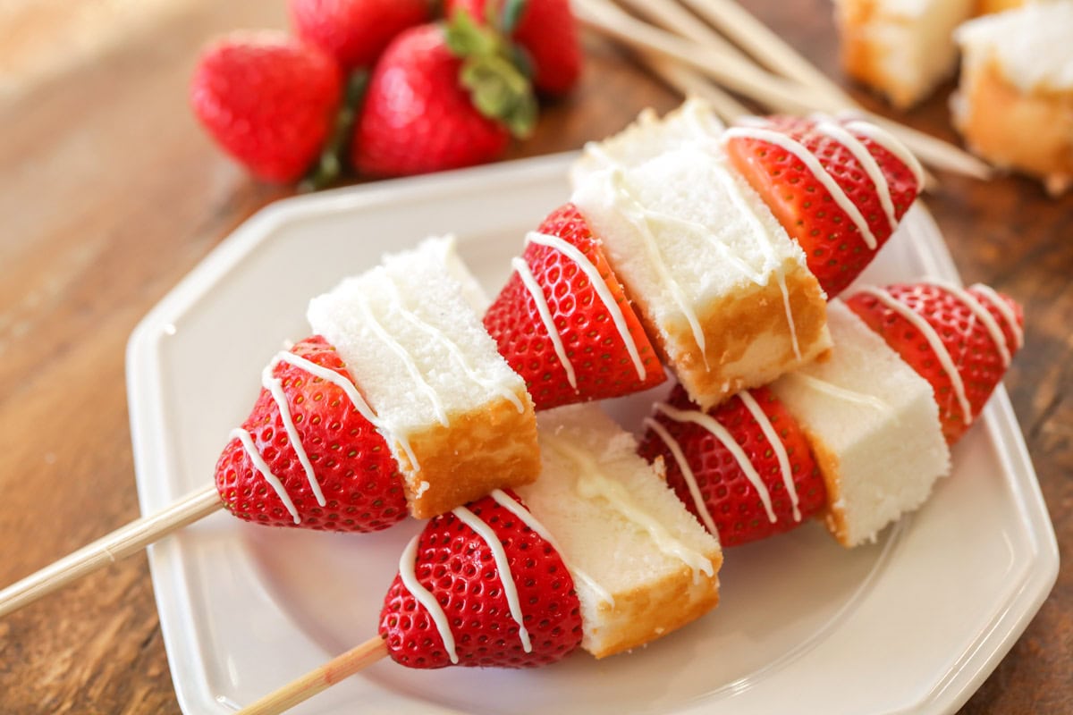 A white plate of strawberry shortcake kabobs.