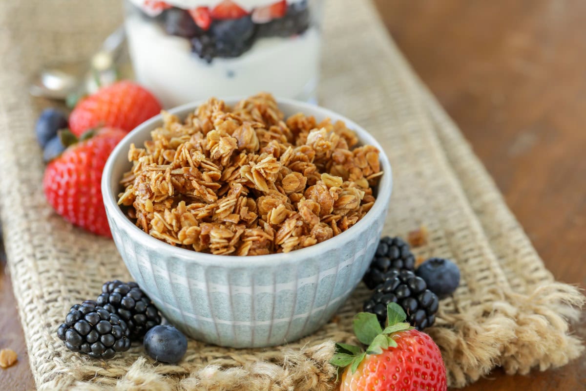 Homemade granola recipe in a blue bowl surrounded by berries.