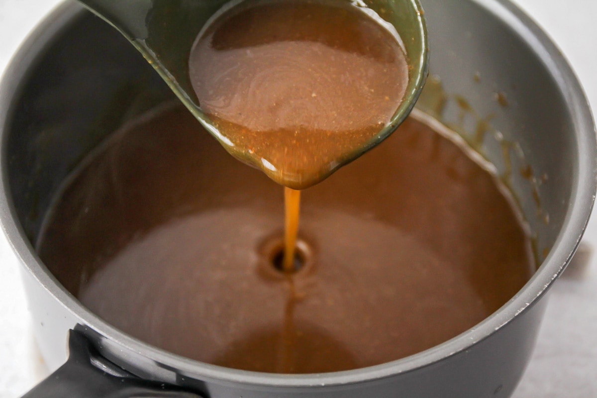 Gravy in a saucepan being scooped with a ladle. 