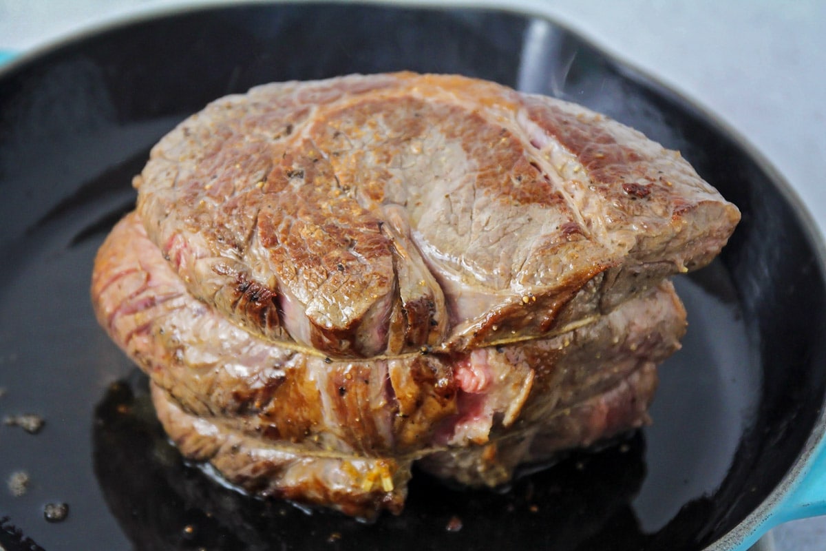 A tied up beef roast being browned in a skillet