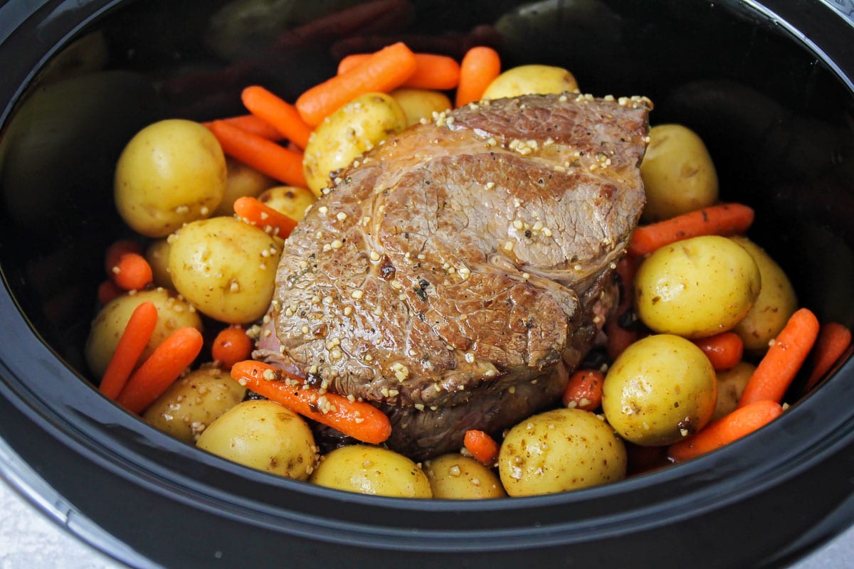 Crock pot filled with ingredients for Pot roast with veggies.