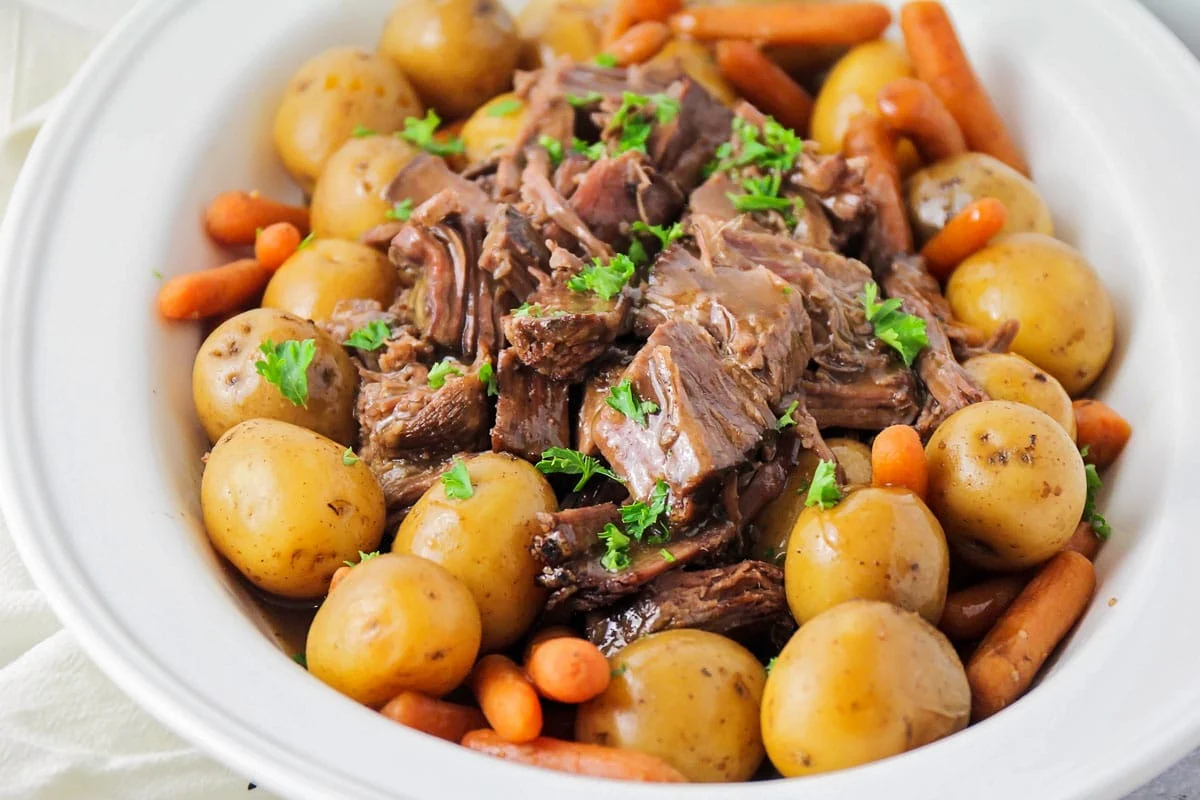 Pot roast and potatoes and carrots in a white bowl.