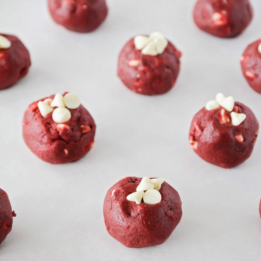 White chocolate red velvet cookie dough balls on a lined baking sheet