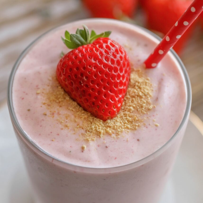 Close up of strawberry cheesecake smoothie topped with graham cracker crumbs and a fresh strawberry