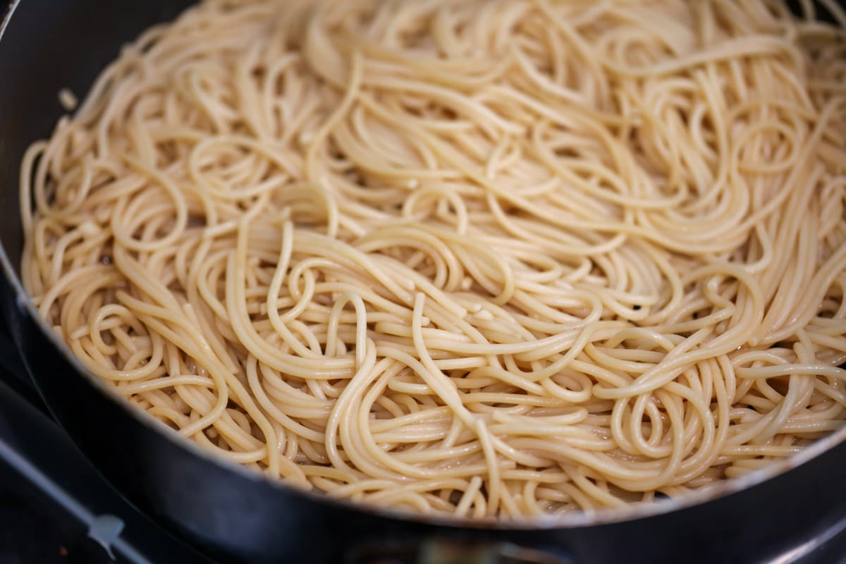 How to make garlic noodles by adding sauce to noodles in a skillet.