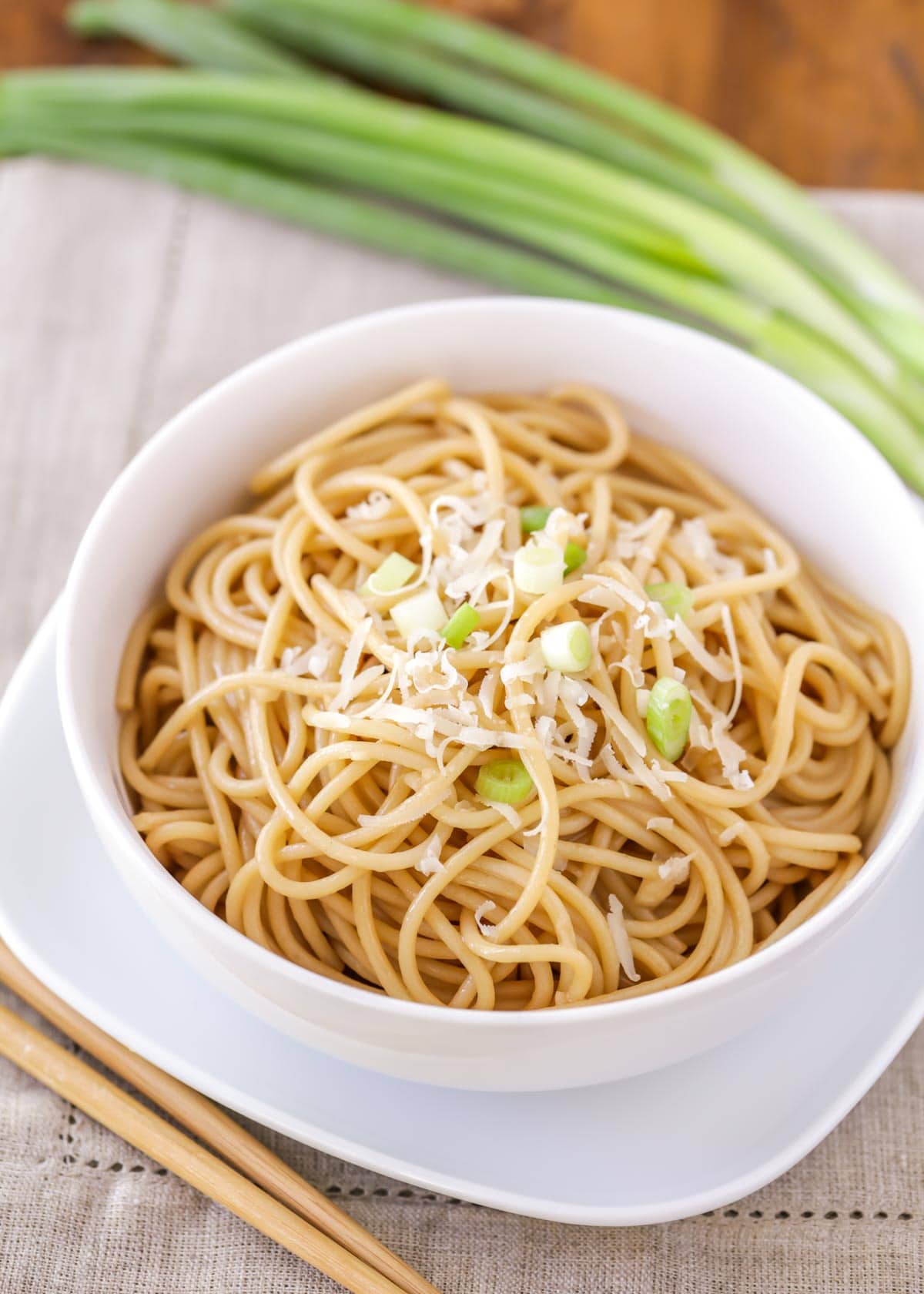 Asian garlic noodles served in a white bowl with parmesan and green onion.