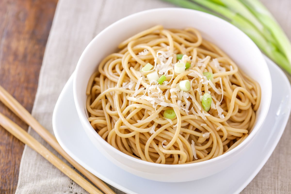 Garlic noodles topped with parmesan and green onions in a white bowl
