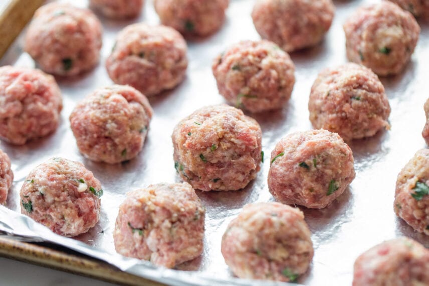 Uncooked homemade meatballs on foil lined baking sheet. 