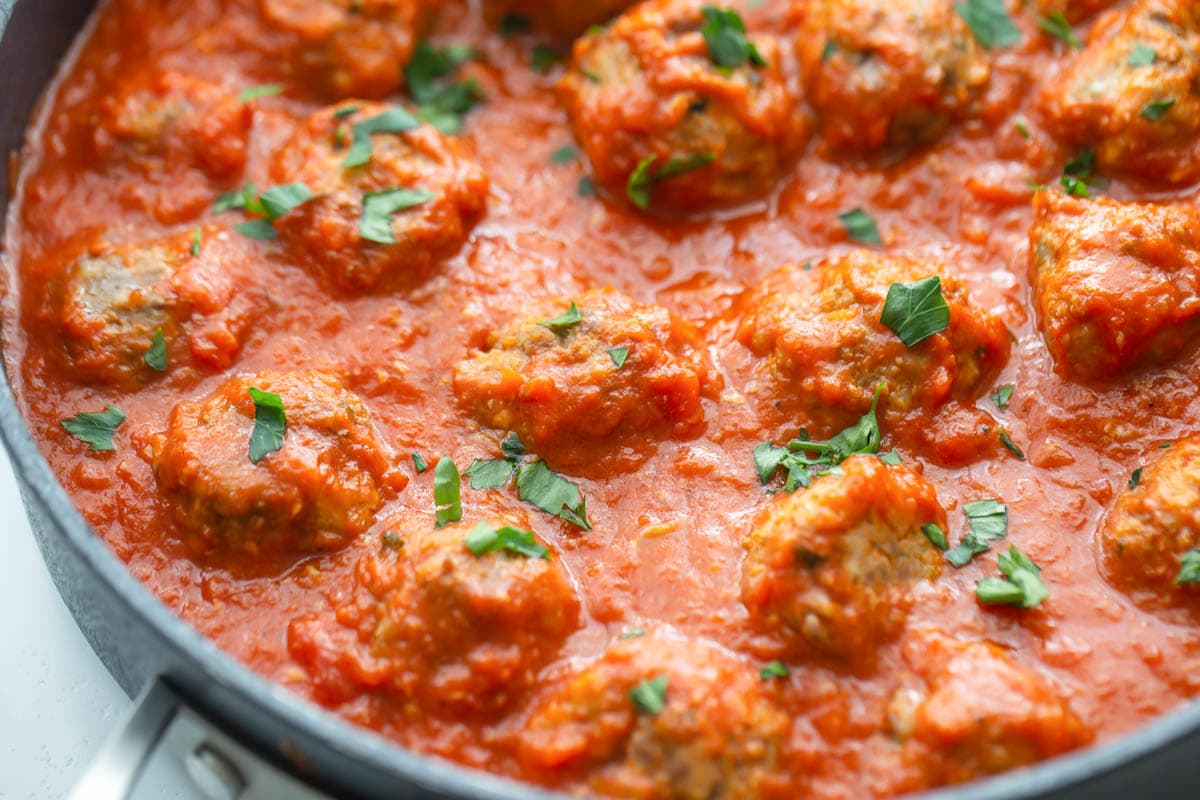 Italian meatballs surrounded with marinara in a skillet.