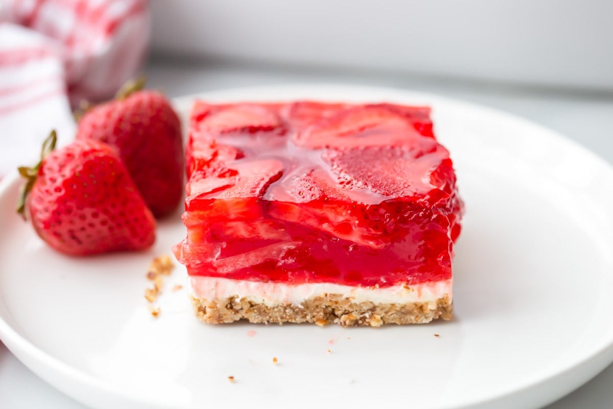 Summer Recipes - A slice of strawberry jello pretzel salad on a plate with two fresh strawberries.