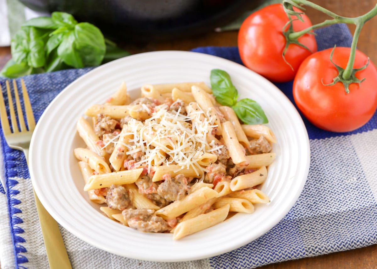 Sausage penne pasta on a white plate with fresh basil leaves.