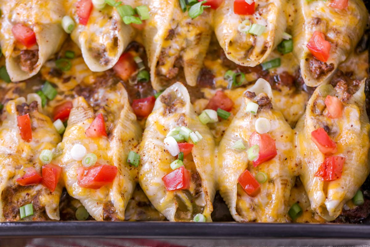 Taco Pasta Shells topped with cheese, diced tomatoes, and green onions.