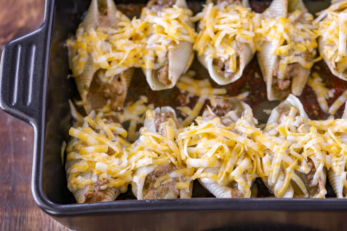 Jumbo pasta shell tacos topped with cheese in a baking dish