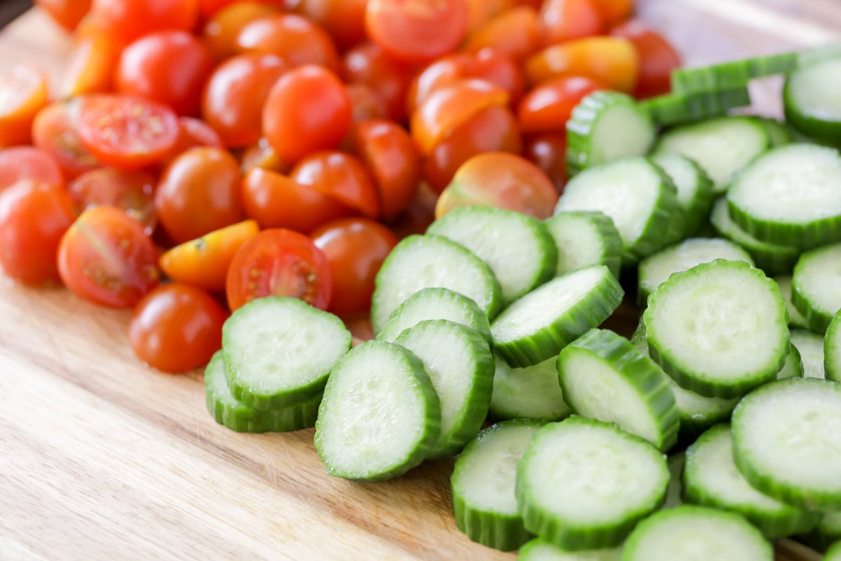 Easy salad recipes - chopped cucumber and tomato on a cutting board. 