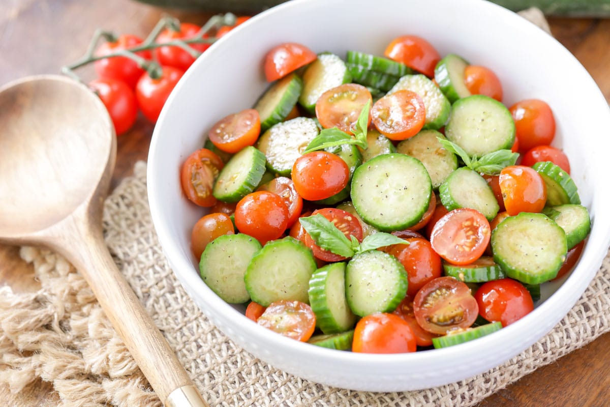 Cucumber tomato salad with fresh basil in a white bowl. 