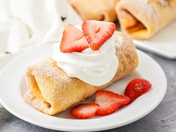 A cheesecake chimichanga served with whipped cream and fresh sliced strawberries.