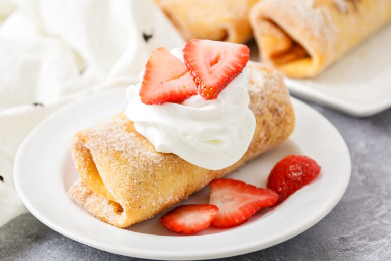 A cheesecake chimichanga served with whipped cream and fresh sliced strawberries.