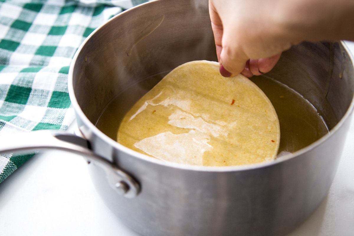 Dipping corn tortilla in enchilada sauce