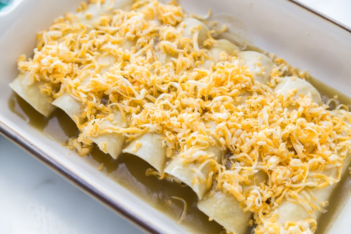 Adding shredded cheese on top of green chile chicken enchiladas