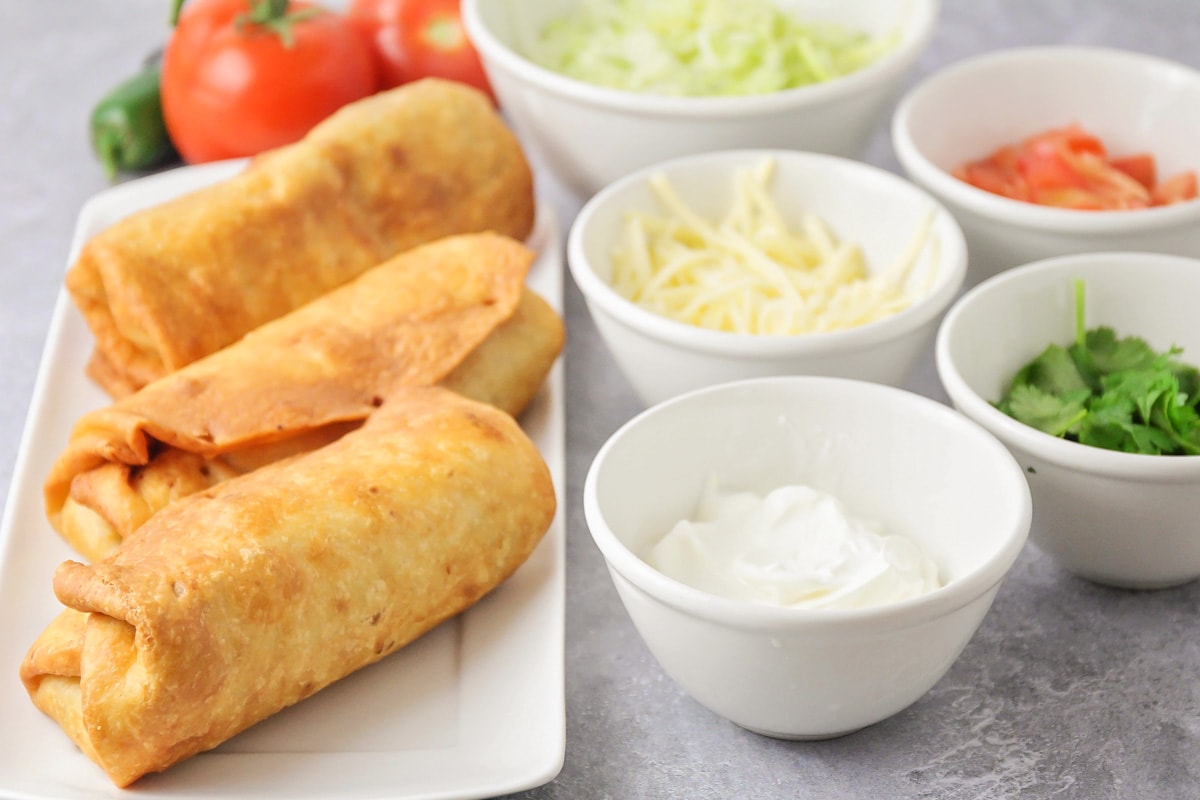 Three fried chimichangas served with toppings.