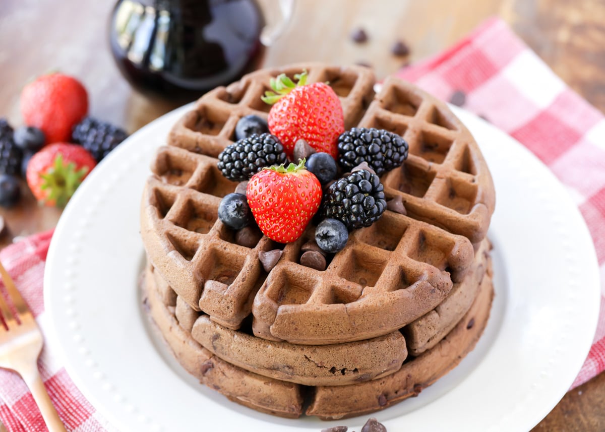 Chocolate waffles topped with fresh berries stacked on a white plate. 