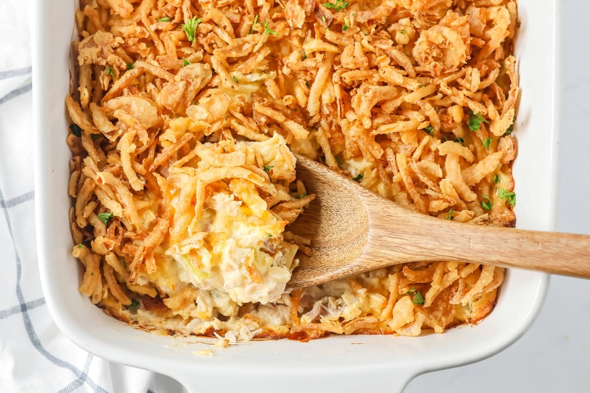 Scooping french onion chicken casserole from a white baking dish.