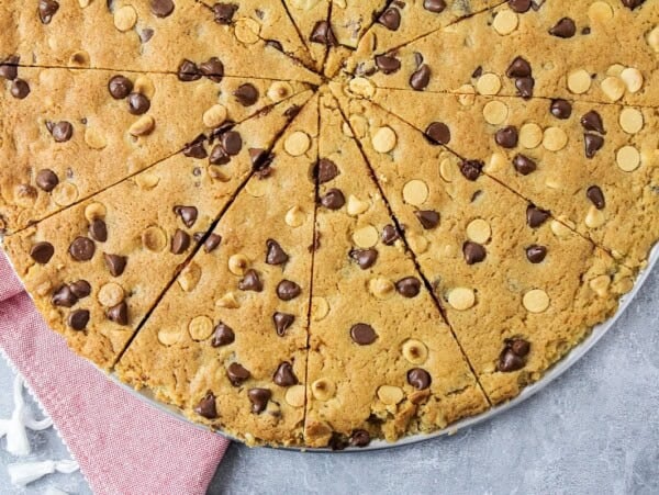 A sliced giant chocolate chip cookie on a pizza plate.